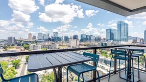 Ein Balkon mit Tisch und Stühlen, mit Blick auf eine Stadtlandschaft mit verschiedenen Gebäuden und blauem Himmel.