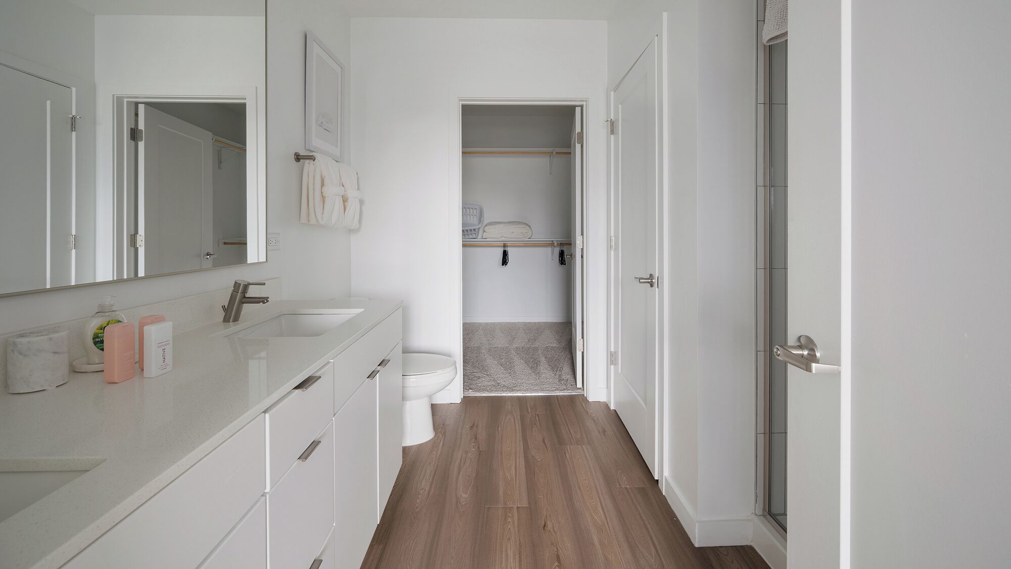 Un bany modern amb un moble de bany blanc, un mirall gran, un vàter i una zona de dutxa.
