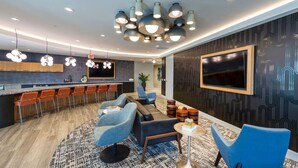 Eine moderne Hotelhalle mit Barbereich, Sitzgelegenheiten und einem großen Bildschirm.