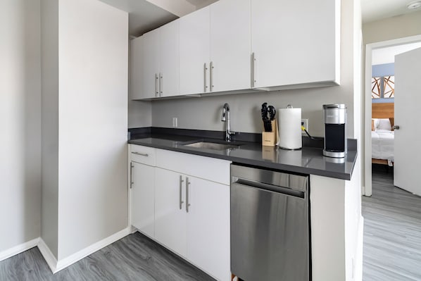 A modern kitchen with stainless steel appliances, a black countertop, and white cabinetry.