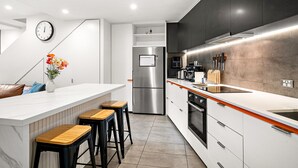 A modern kitchen with a central island, stainless steel appliances, and a clock on the wall. - Modern Carlton Living Minutes to CBD (Melbourne)