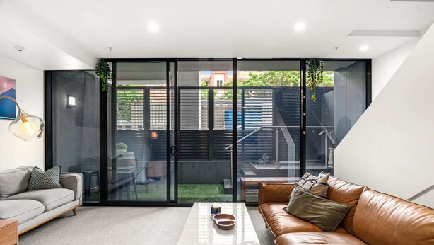 A modern living room with a glass door leading to a balcony, a sofa, a coffee table, and a small side table. - Modern Carlton Living Minutes to CBD (Melbourne)