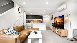 A modern living room with a leather sofa, a coffee table, a TV, and a bookshelf. - Modern Carlton Living Minutes to CBD (Melbourne)