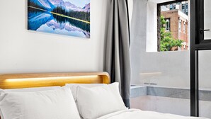 A hotel room with a bed, a painting of a mountain landscape, a view of a building through a window, and a curtain. - Modern Carlton Living Minutes to CBD (Melbourne)