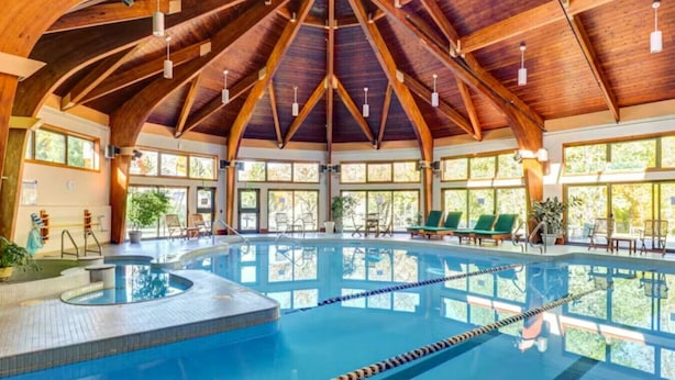 An indoor swimming pool with a wooden ceiling and large windows. - Hilltopper Haus- Pool, hot tub, Private Sauna (Killington)