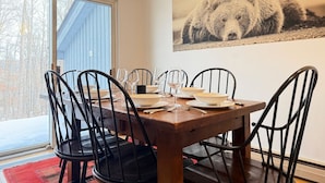 A dining area with a wooden table set for six, black metal chairs, and a large bear painting on the wall. - Hilltopper Haus- Pool, hot tub, Private Sauna (Killington)