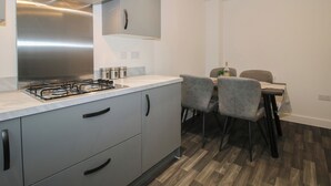 Una cocina moderna con campana extractora de acero inoxidable, gabinetes grises y un comedor con mesa y sillas.
