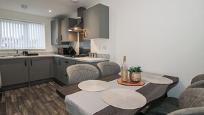 Una cocina moderna con armarios grises, estufa empotrada y comedor con mesa de madera oscura y sillas grises.