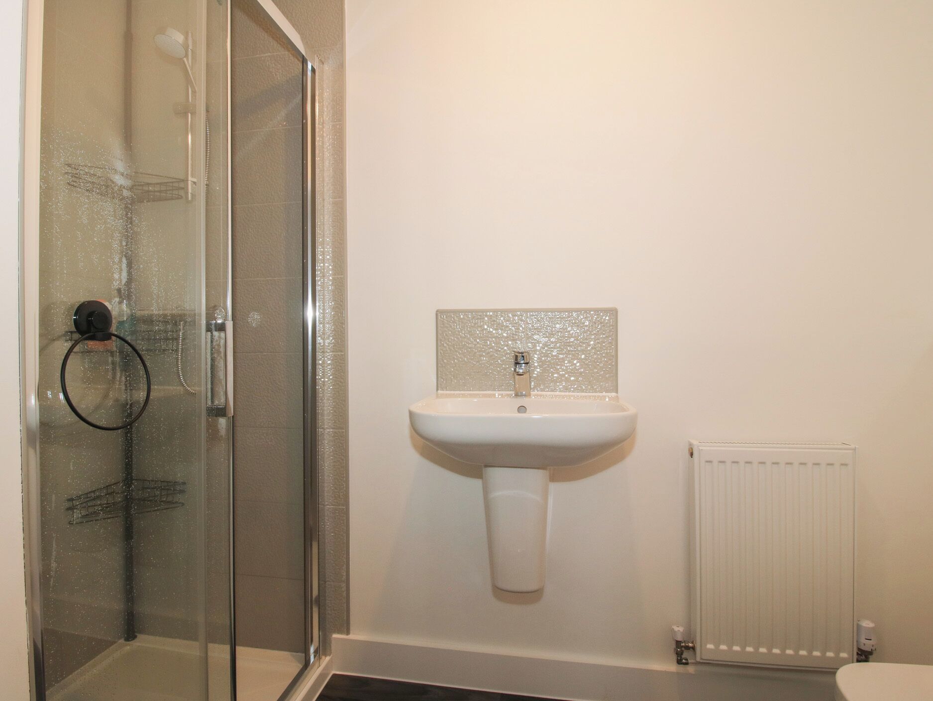 Une salle de bain avec une douche à parois de verre, un lavabo blanc avec un pare-éclaboussures texturé et un radiateur blanc.