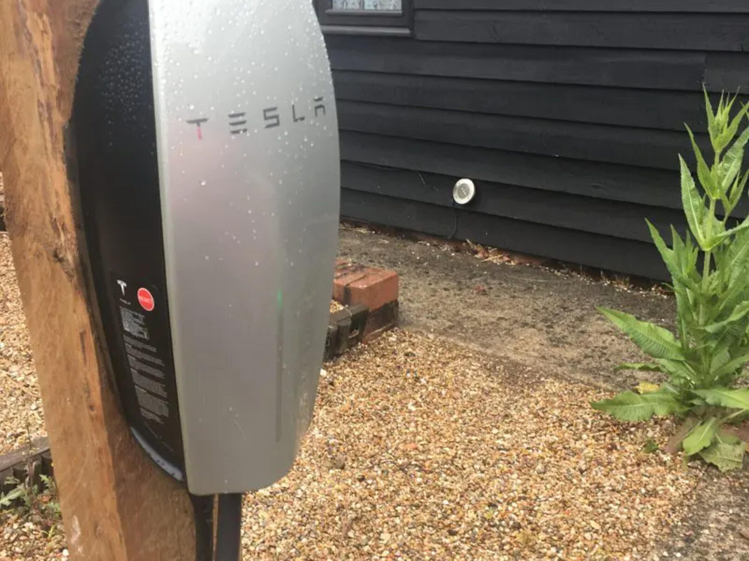 Una colonnina di ricarica per veicoli elettrici Tesla con vialetto sterrato e palo di legno.