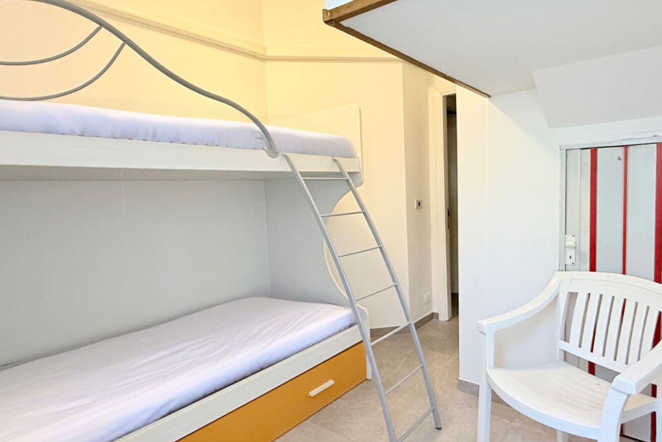 Een stapelbed met een ladder, een witte stoel en een deur met rode strepen.