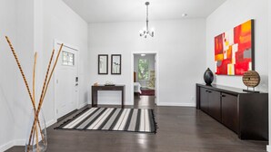 Un couloir moderne avec un parquet en bois foncé, un tapis à rayures, une console sombre et un grand tableau abstrait accroché au mur.