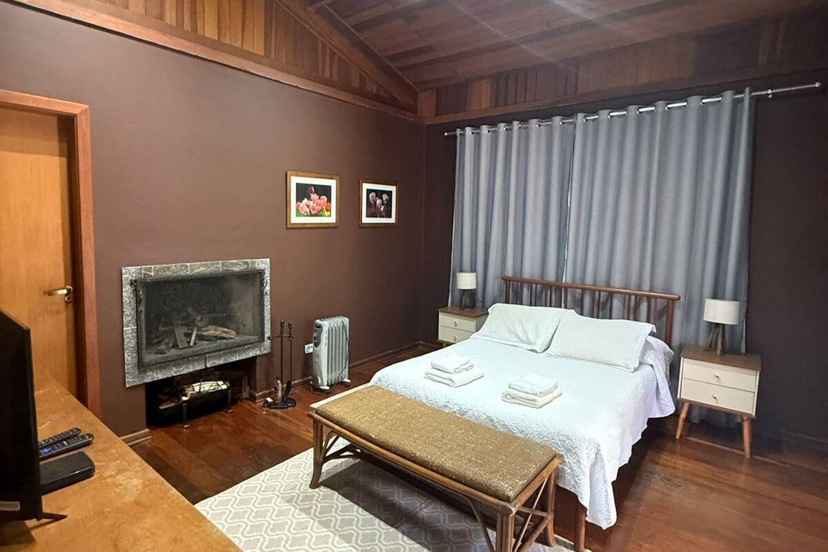 Ein Schlafzimmer mit Bett, Nachttischen, Kamin, Fernseher und einer Holzbank.