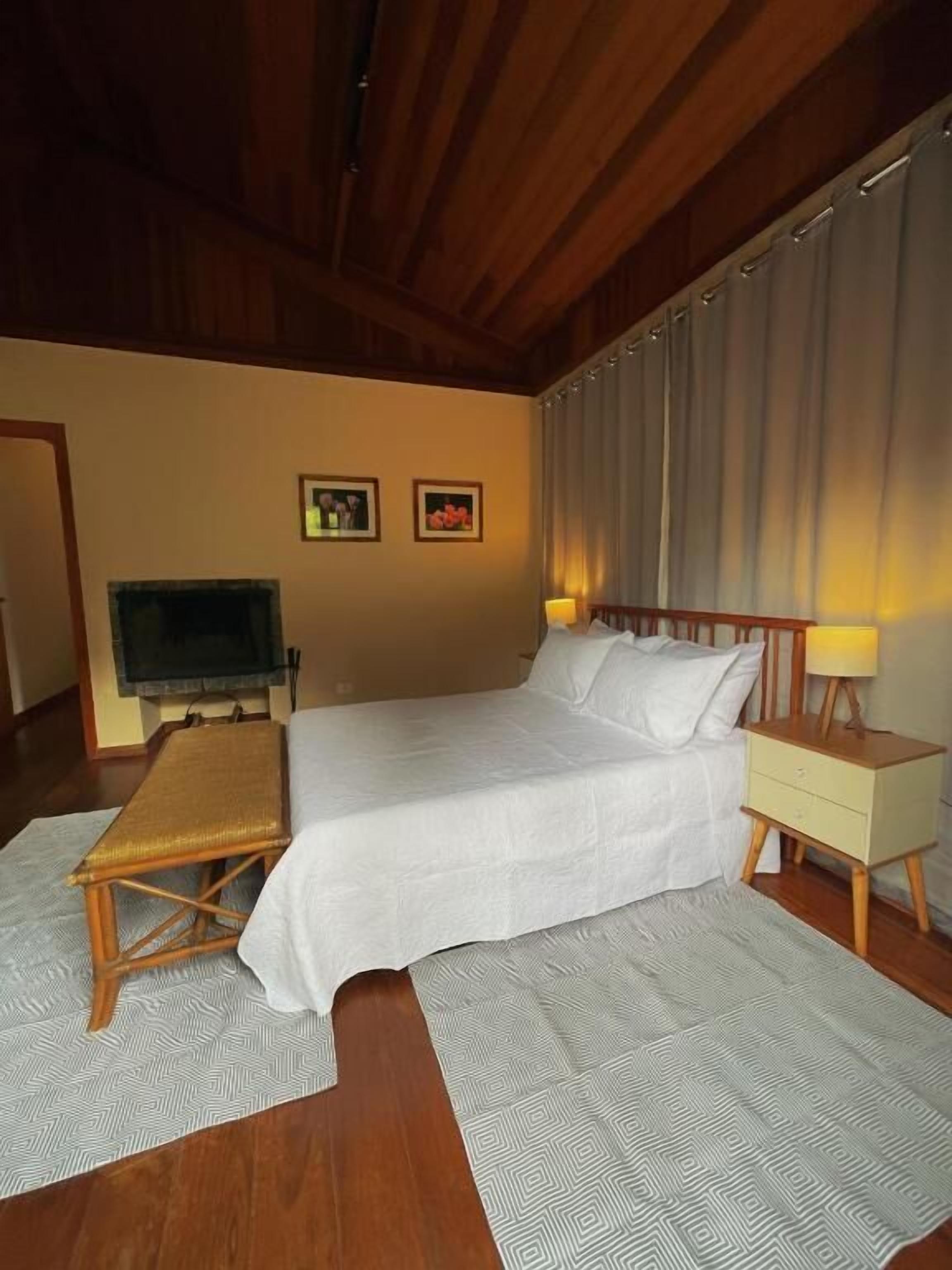 A bedroom with a bed, bedside tables, a bench, a TV, and two framed pictures on the wall.