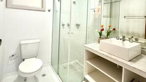 Une salle de bain moderne avec une douche à parois de verre, des toilettes blanches et un grand miroir au-dessus du lavabo.