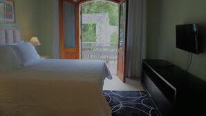 Une chambre d’hôtel avec un lit, une télévision et un balcon donnant sur un espace verdoyant.