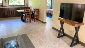 A spacious living area with a kitchen, dining table, and a TV on a wooden stand. - Nature and Beach (Coco)