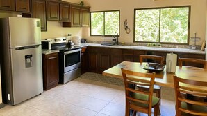 A kitchen with dark wooden cabinets, a stainless steel refrigerator, an oven, and a dining area with a table and chairs. - Nature and Beach (Coco)