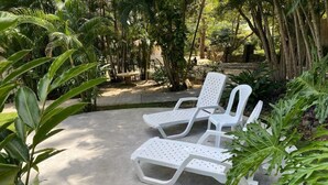 Two white lounge chairs with perforated backs and seats, positioned on a concrete surface surrounded by lush greenery and trees. - Nature and Beach (Coco)