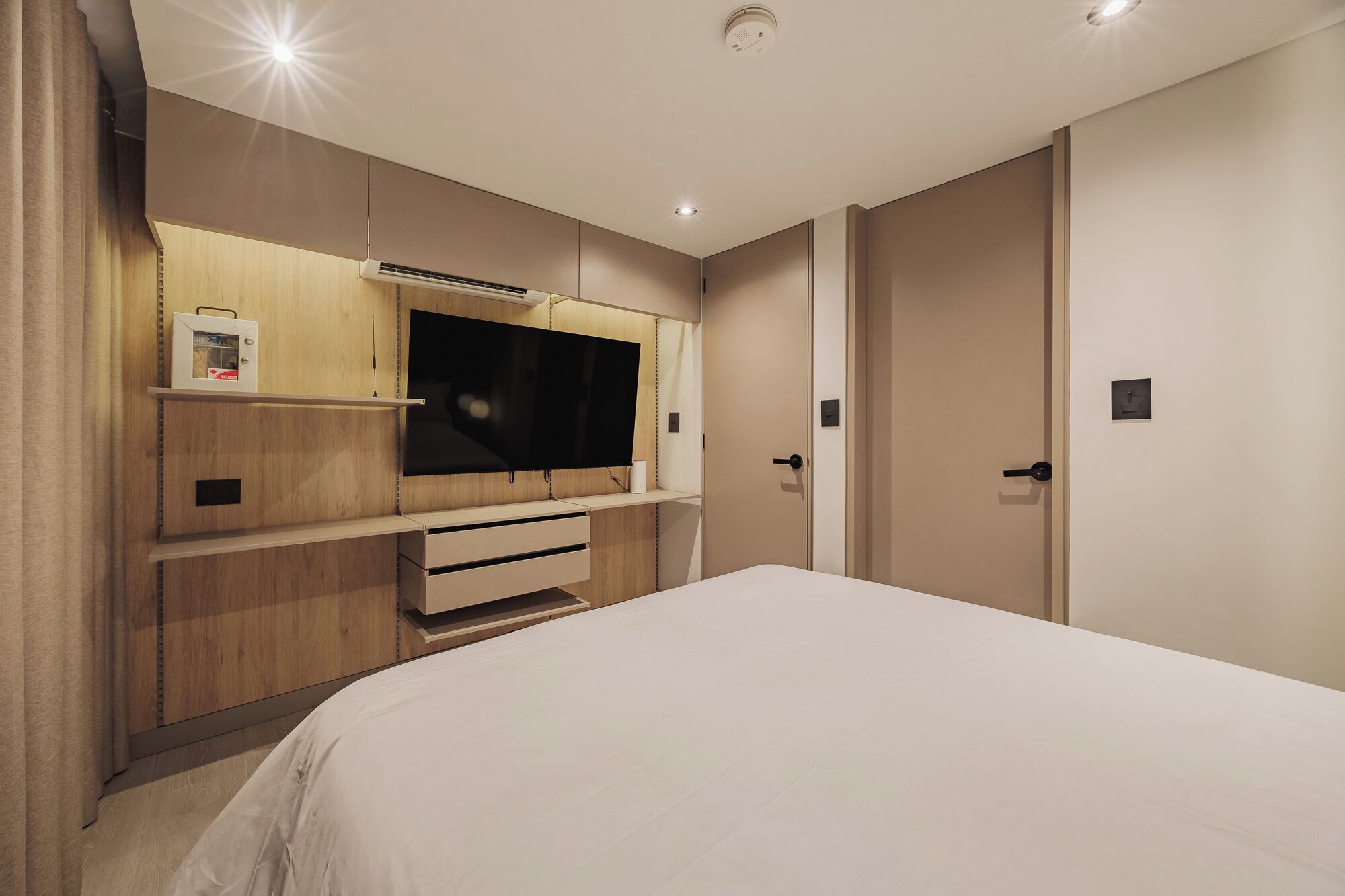 A bedroom with a large bed, a TV mounted on a wooden cabinet, and a door with a handle.