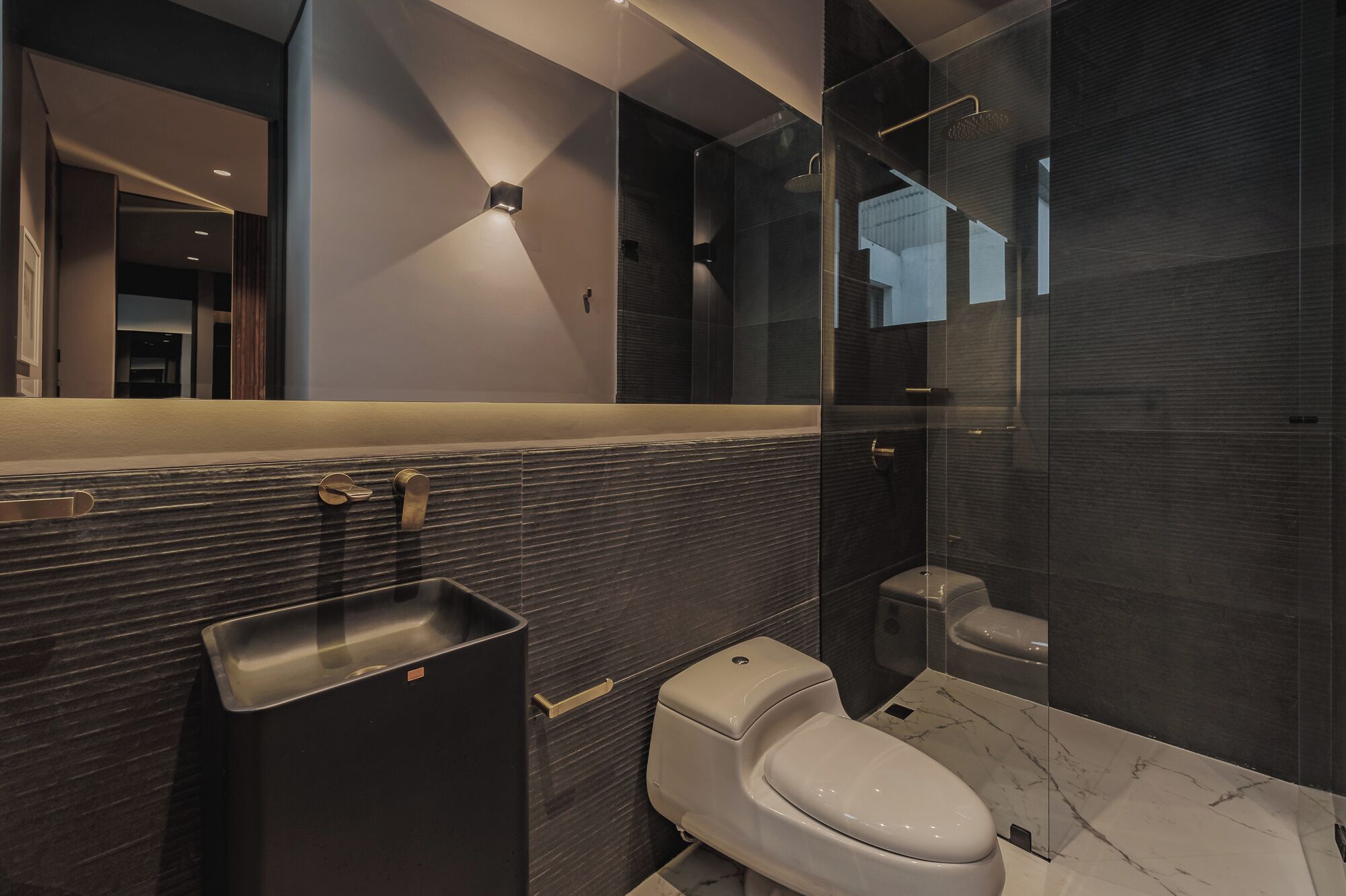 A modern bathroom with a marble sink, a toilet, and a glass-enclosed shower area.