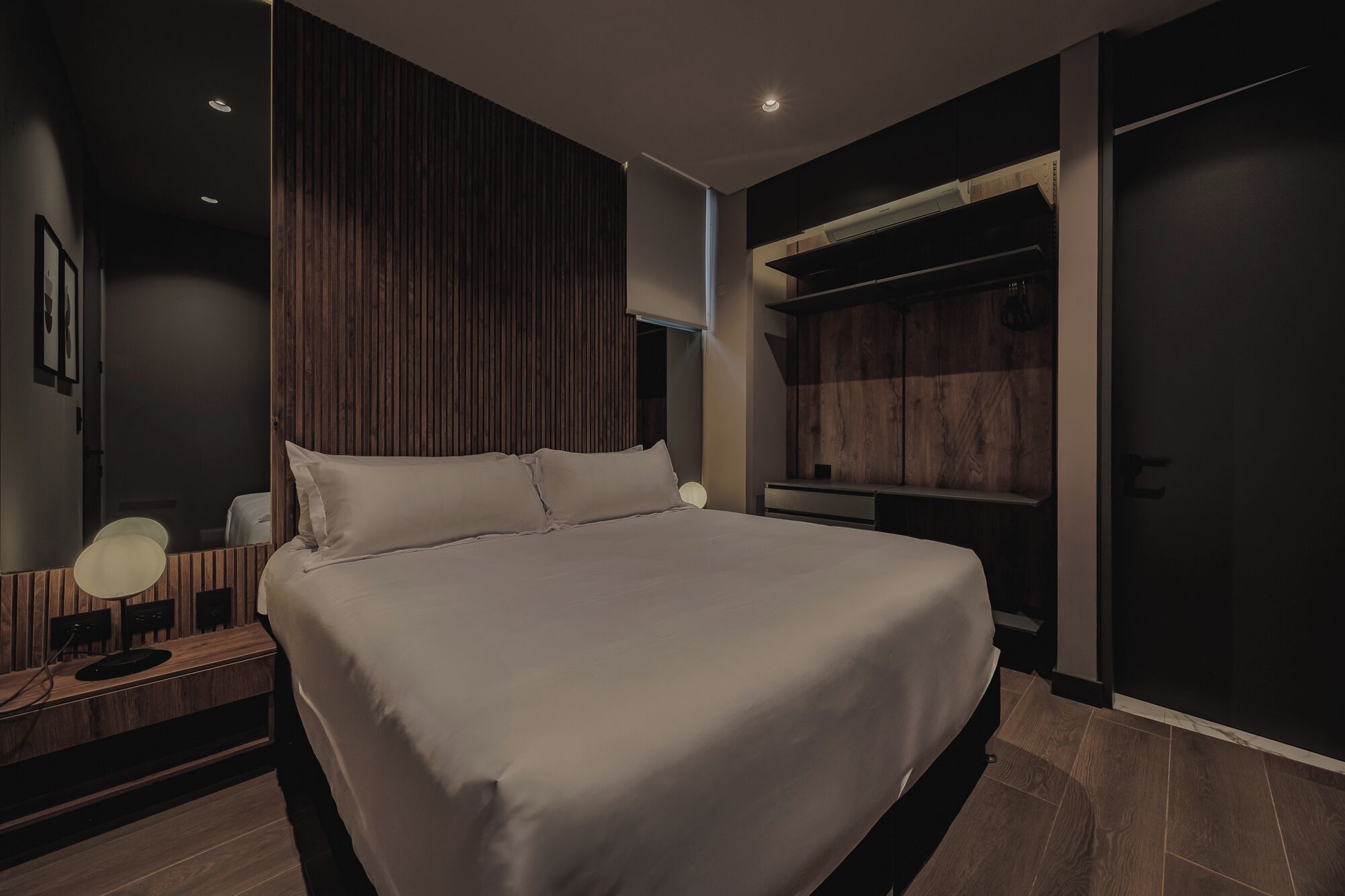 Une chambre moderne avec un grand lit, une table de chevet avec une lampe, une armoire et un placard intégré avec espace pour suspendre les vêtements.