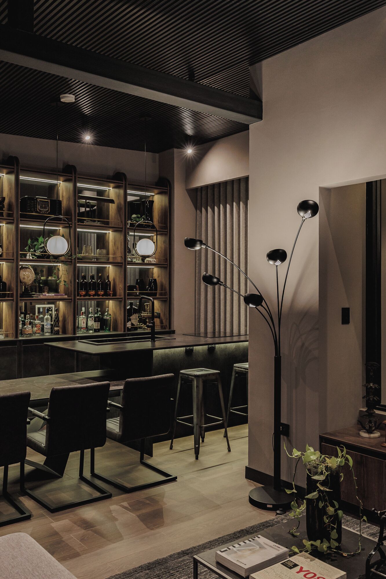 A modern bar area with a dark wood ceiling, bar stools, and a variety of bottles and glasses on shelves.