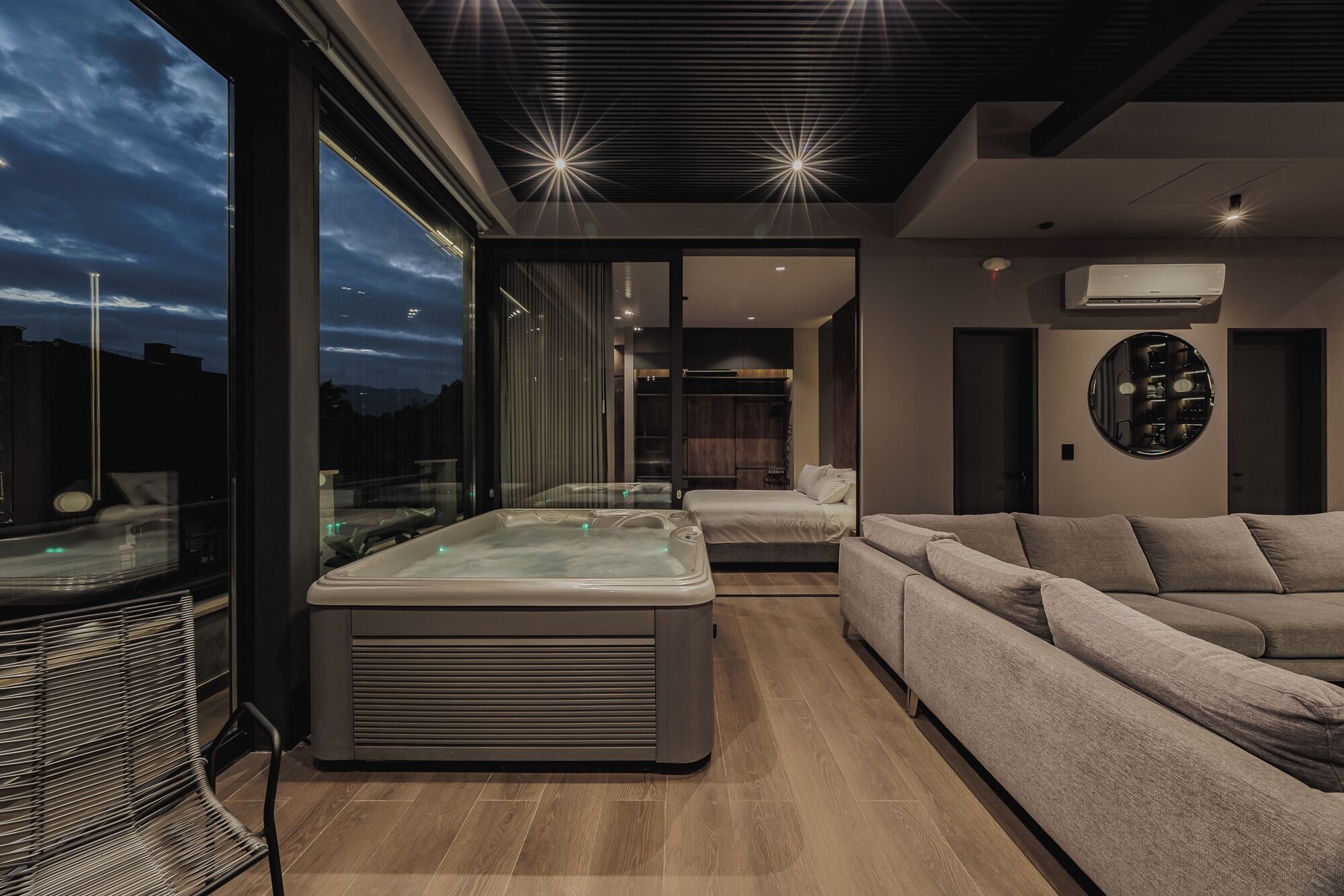 Un intérieur moderne avec une grande baie vitrée, un jacuzzi, un canapé et un grand miroir rond accroché au mur.