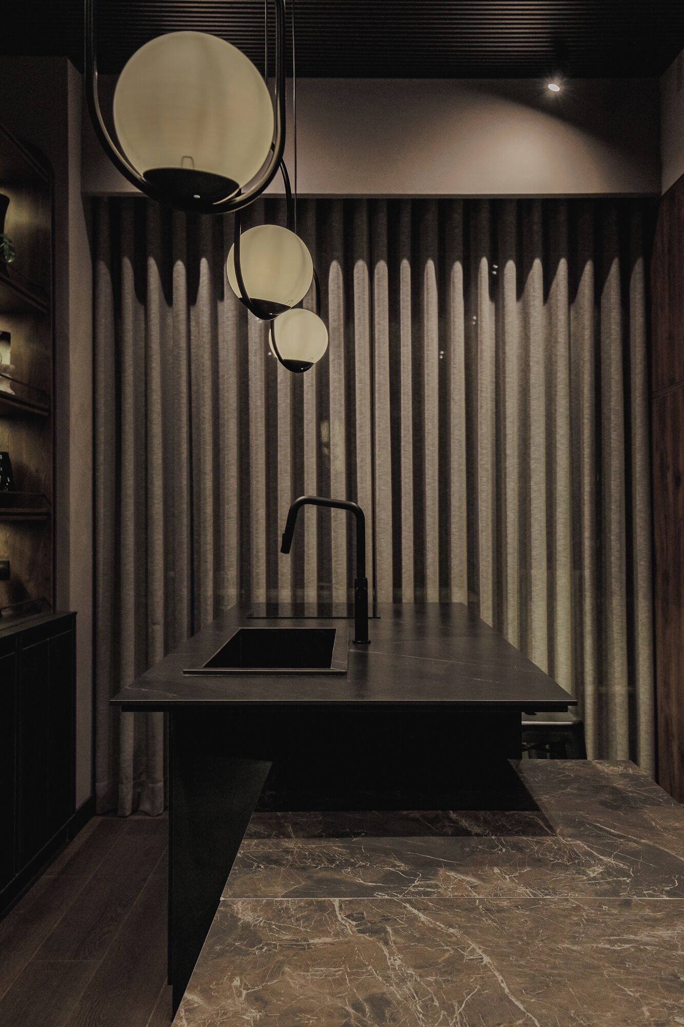 Een moderne badkamer met een donker marmeren aanrechtblad, een zwarte wasbak en een bijzondere lamp erboven.