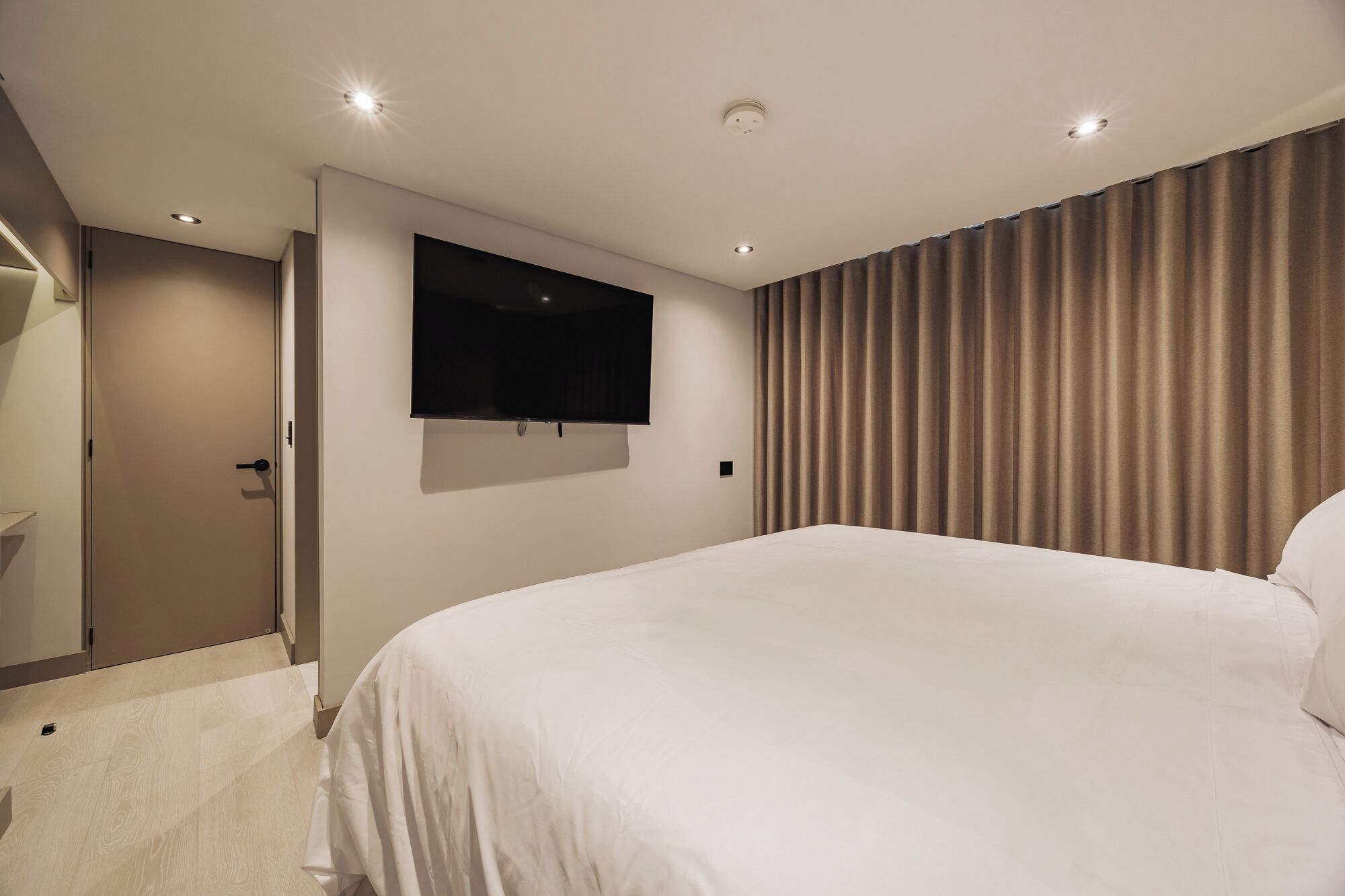 Et moderne hotelværelse med en stor seng, et fladskærms-tv på væggen og en dør til et badeværelse.