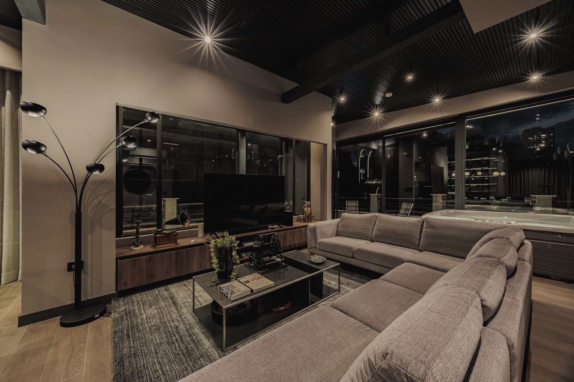Uma sala de estar moderna com uma grande TV de tela plana, um sofá, uma mesa de centro e uma janela grande com vista para a cidade.