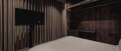 Une chambre moderne avec un grand lit, un téléviseur à écran plat fixé au mur et une armoire dotée d’étagères intégrées.