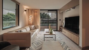 A modern living room with a sofa, a coffee table, a TV, and a balcony with curtains. - Revellion by EP (Medellín)