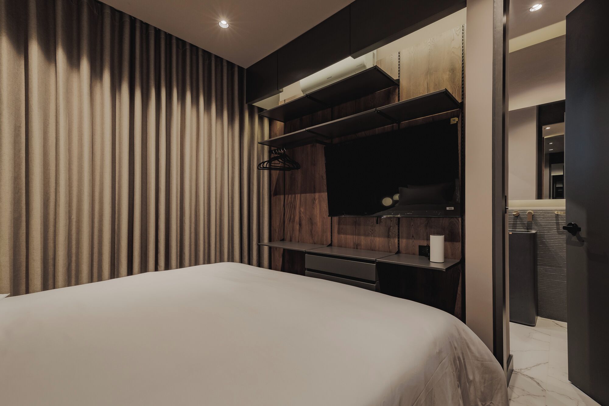 Una habitación de hotel moderna con una cama grande, un televisor integrado y una pared de paneles de madera.