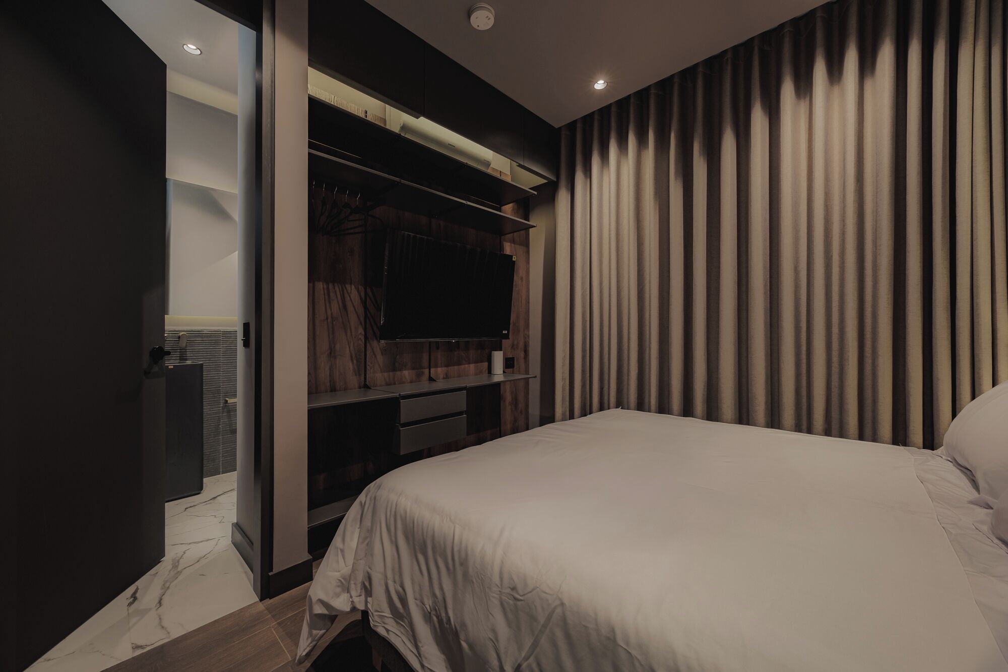 A modern bedroom with a large bed, built-in TV, and a walk-in closet.