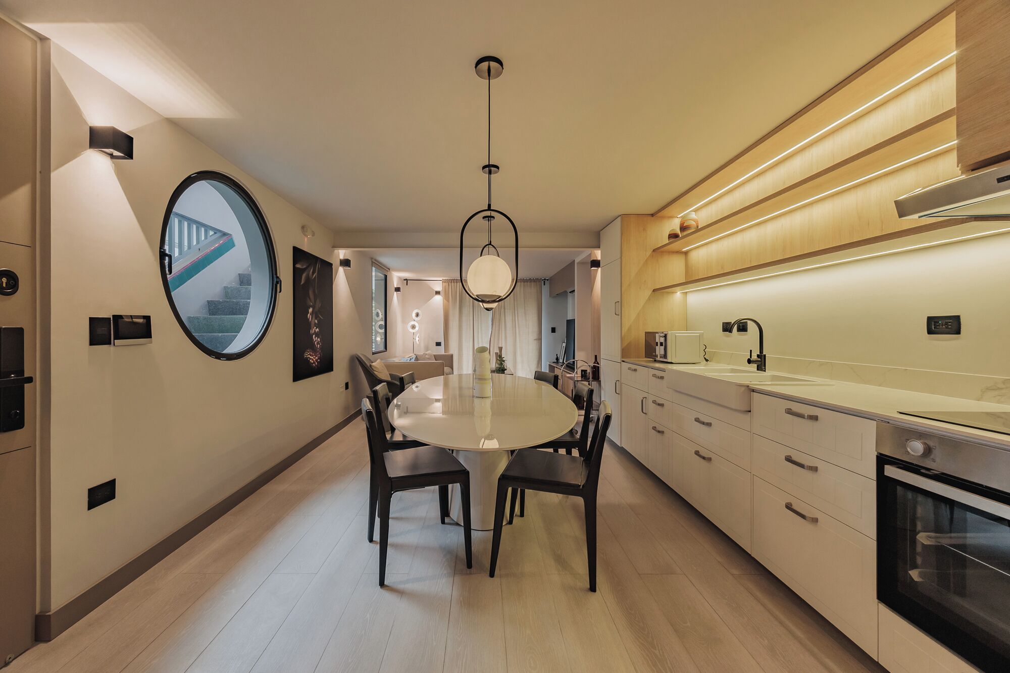 Een moderne keuken met een centraal eiland, een eetgedeelte met een ronde tafel en uitzicht op een trap.