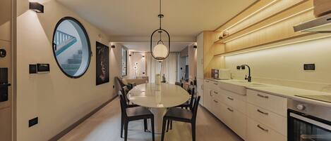 Een moderne keuken met een centraal eiland, een eetgedeelte met een ronde tafel en uitzicht op een trap.