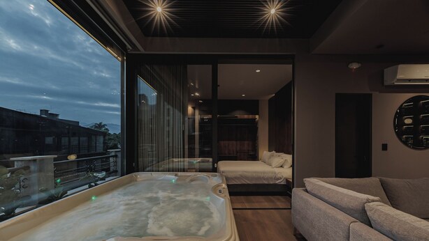 A modern bedroom with a large window, a sofa, a bed, and a hot tub. - Revellion by EP (Medellín)