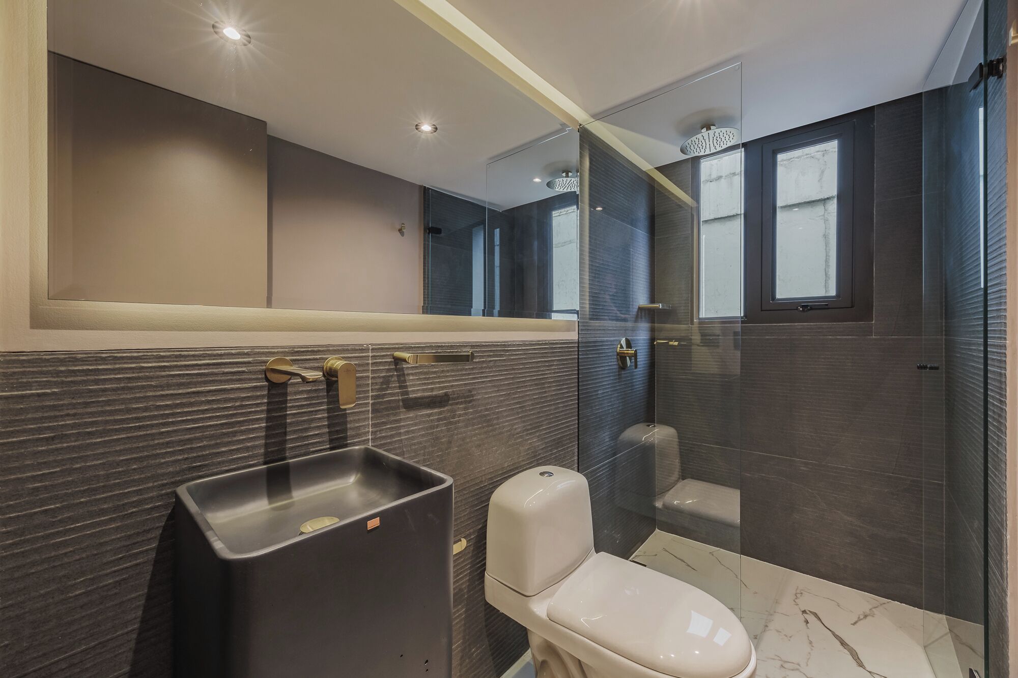Un baño moderno con un espejo grande, un inodoro y una zona de ducha.