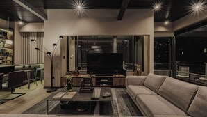 A modern living room with a sofa, coffee table, and TV. There is a bar area with stools and a shelf with bottles. - Revellion by EP (Medellín)