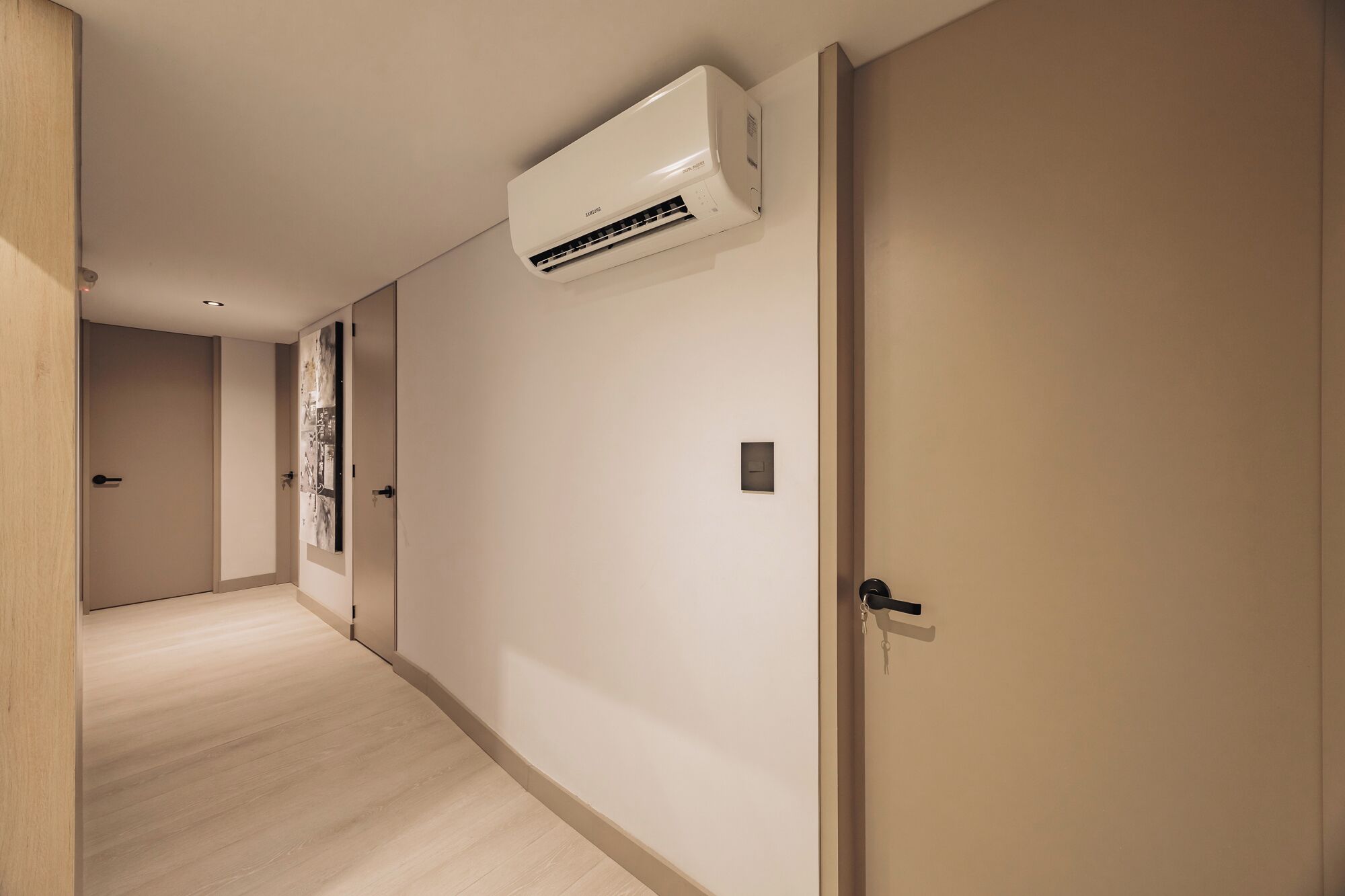 A hallway with a wall-mounted air conditioner, a door with a keyhole, and a light switch.
