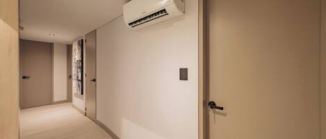 Un pasillo con un aire acondicionado de pared, una puerta con mirilla y un interruptor de luz.