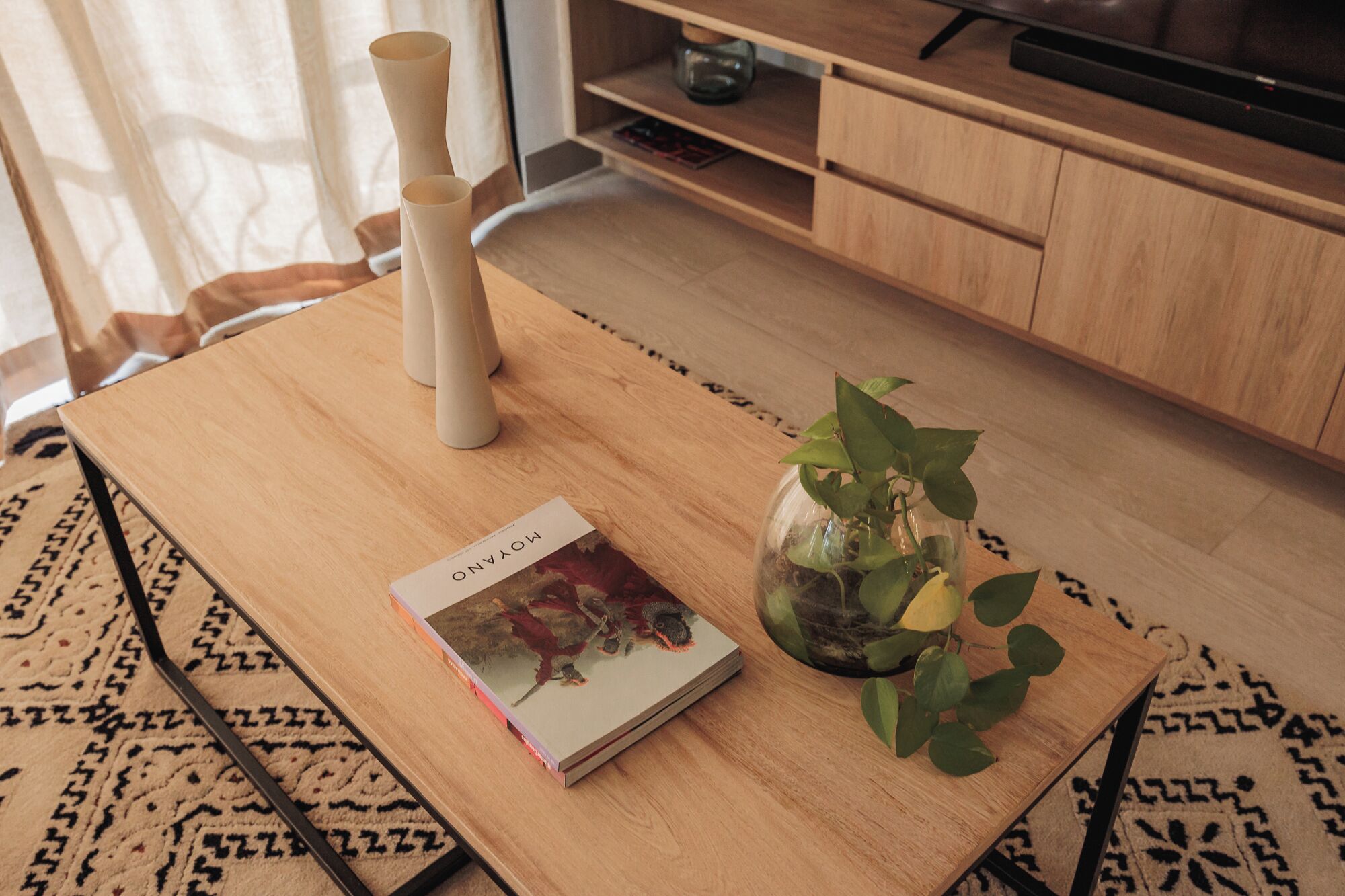 A wooden table with a book titled 'MOTANO' and a glass vase with a plant.