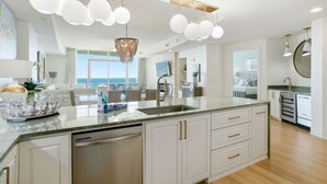 A modern kitchen with a large island, stainless steel appliances, and pendant lighting. - Turquoise D1005 (Orange Beach)