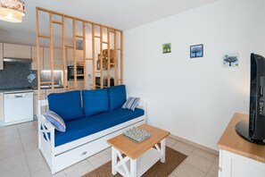 A modern living room with a blue sofa, a wooden coffee table, and a TV on a stand. - Côte Fleurie · Cosy Norman apt, balcony & parking (Saint-Arnoult)