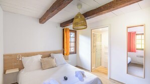 Ein gut beleuchtetes Schlafzimmer mit einem hölzernen Kopfteil, einem Bett mit weißen Laken, einem Nachttisch und einem großen Spiegel an der Wand.