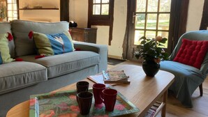 Ein gemütliches Wohnzimmer mit einem grauen Sofa, einem Holztisch und einem blauen Sessel. Ein Fenster bietet Blick auf Grünfläche.