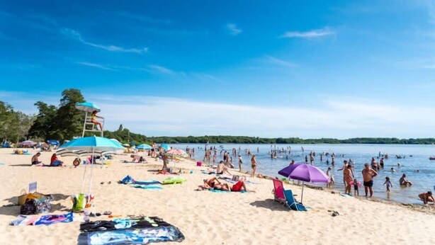 Ein Strand mit badenden Personen, Sonnenschirmen und einem Rettungsturm.