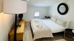 Een slaapkamer met een bed, nachtkastje, lamp, spiegel en raam.