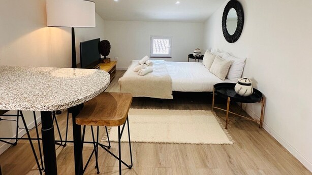 Een moderne slaapkamer met een bed, nachtkastje, lamp en een ronde tafel met stoelen.